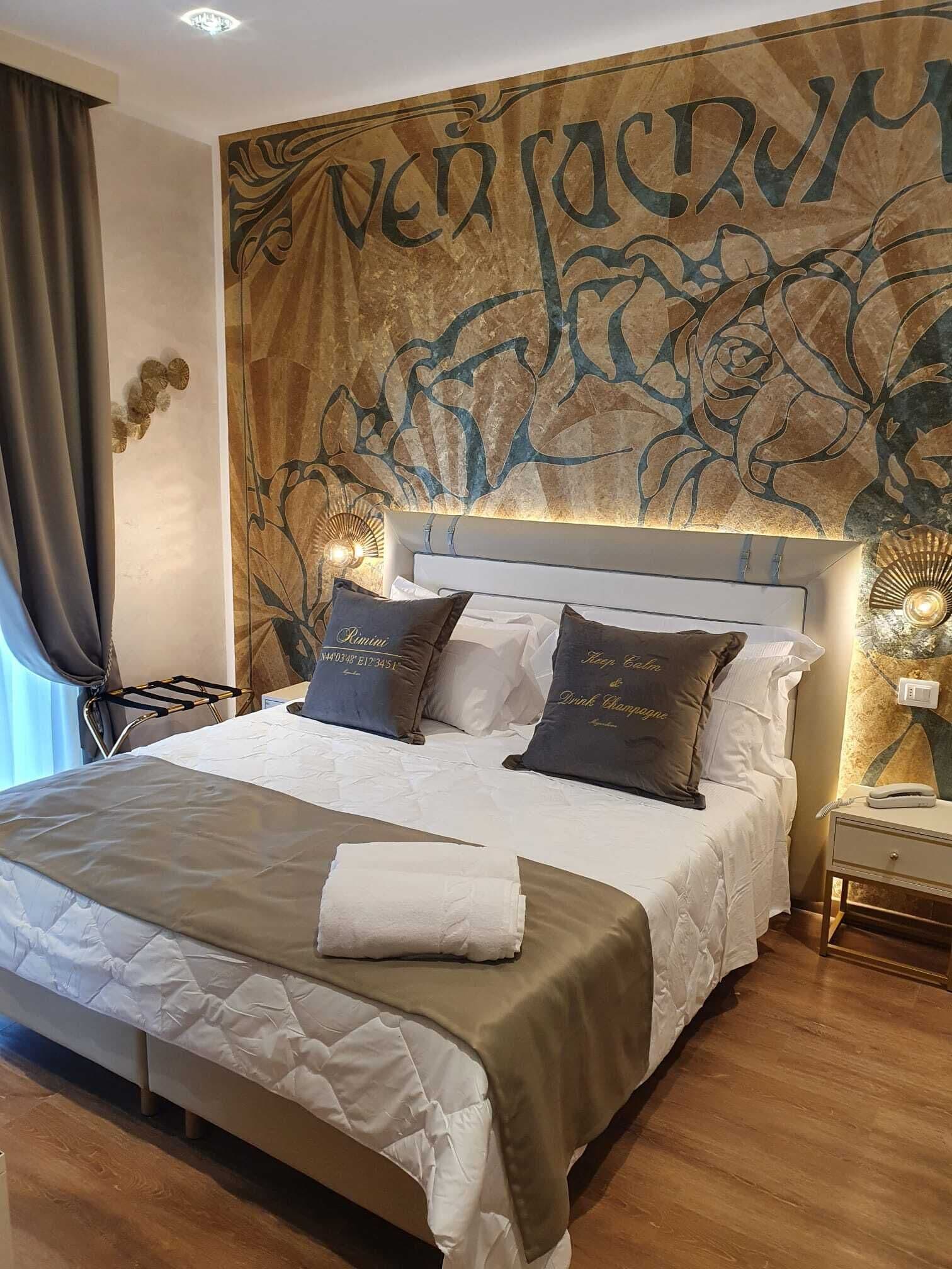 A neatly made bed with a white and beige bedspread, two pillows with text, a bedside table with a lamp, and a wall with a floral pattern.