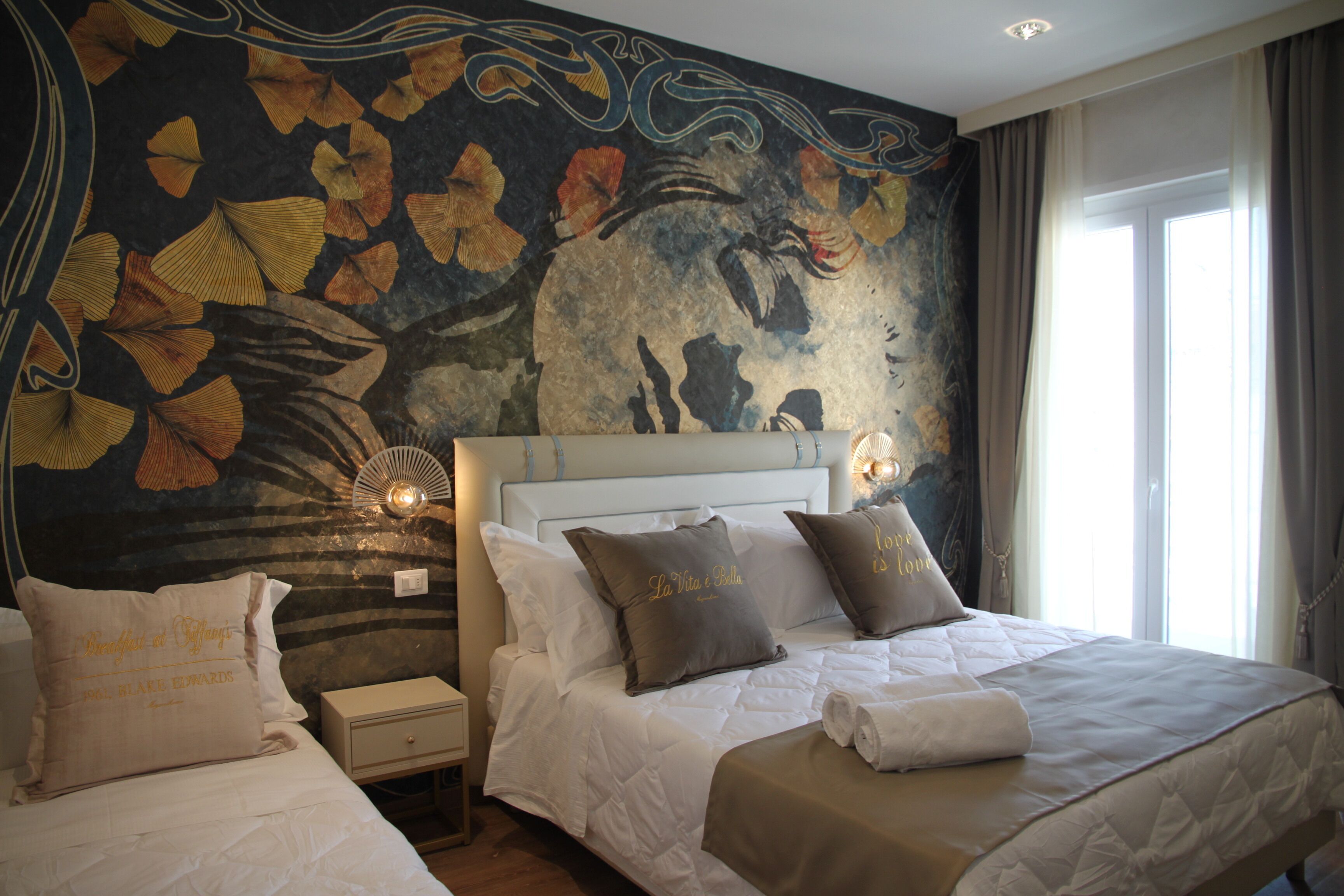 A hotel room with two beds, a mural on the wall, and a window with curtains.