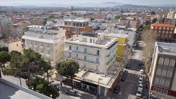 Hotel de vários andares com terraço no telhado, situado numa área urbana densamente construída.