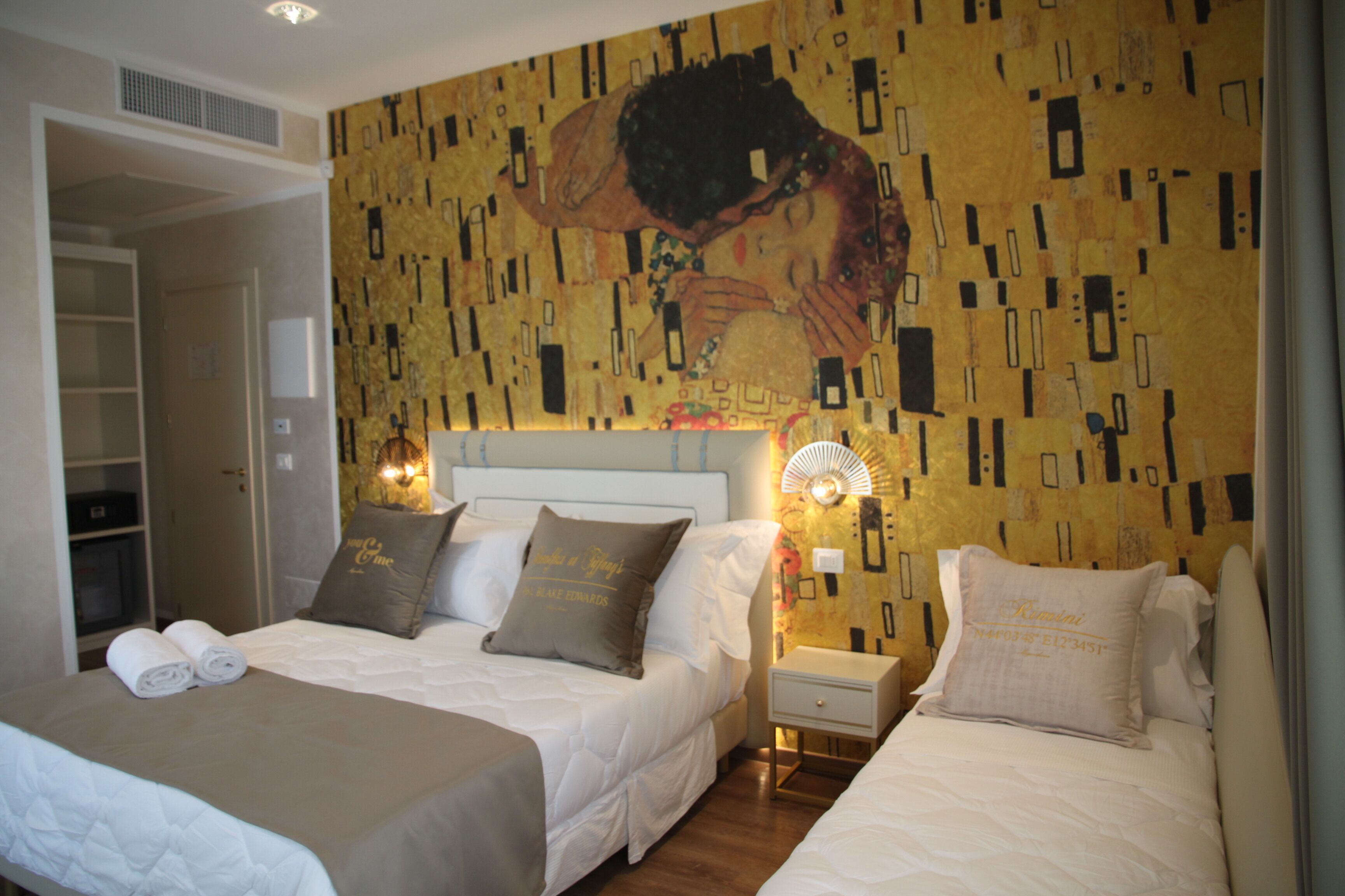 A hotel room with two beds, a large painting on the wall, and a bedside table with a lamp.