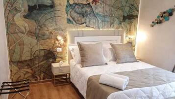 A bedroom with a large mural on the wall, a bed with a beige and white duvet, a nightstand with a lamp, and a wooden floor.