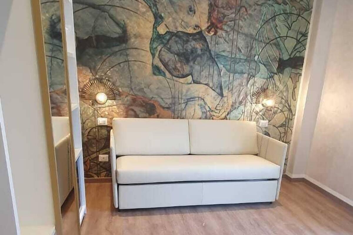 A room with a white sofa, a wooden floor, and a large abstract mural on the wall.
