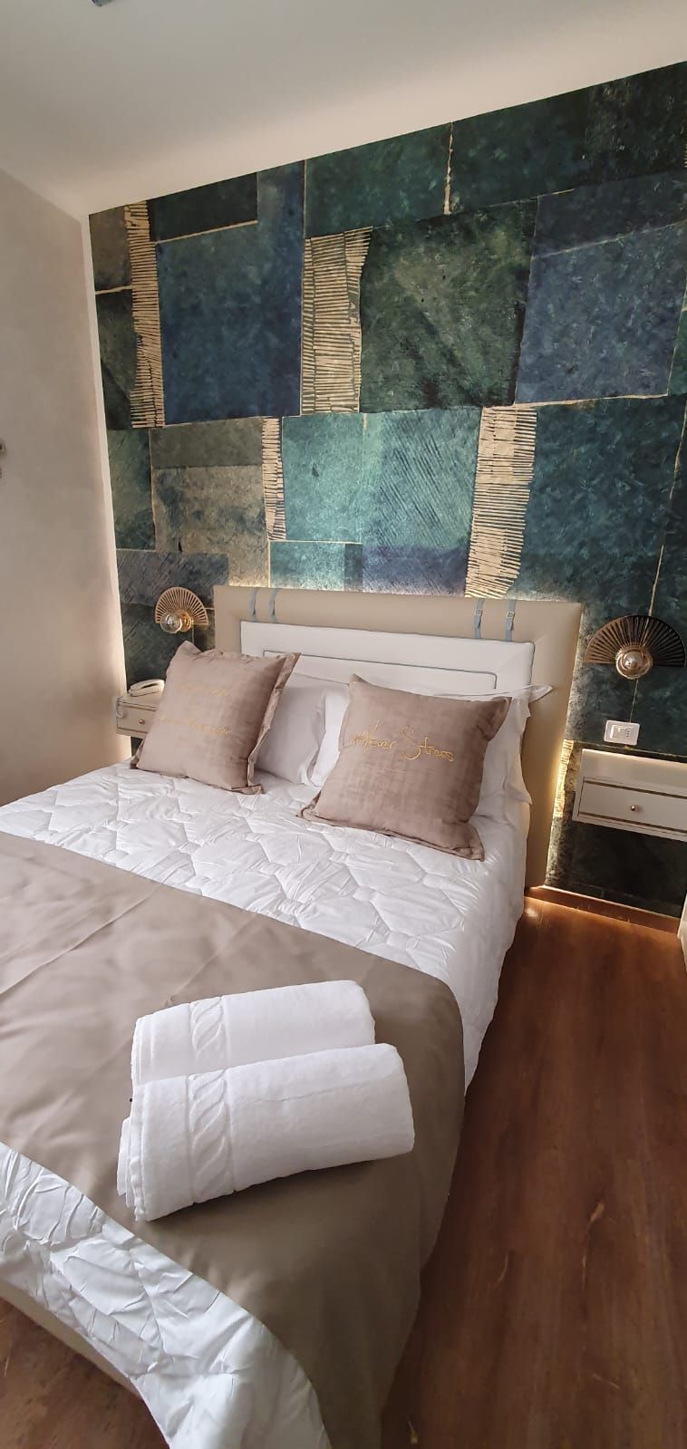 A bed with a quilted white duvet, two pillows, and a folded white towel on the side.