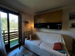Quarto com cama, radiador, estante com livros e janela com vista para áreas verdes.