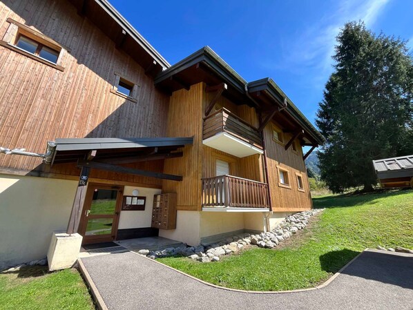 A two-story wooden building with a balcony, a stone pathway, and a grassy area.