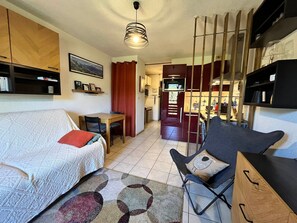 A compact living space with a sofa, a dining table, a chair, and a kitchenette area.