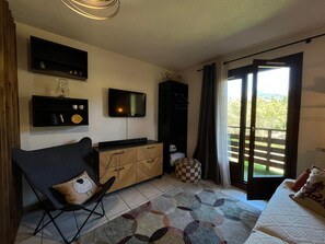 Une chambre à coucher comprenant un lit, une télévision, un bureau, une chaise, une armoire, une fenêtre et une vue sur la verdure.
