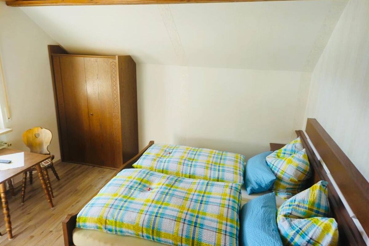 A bedroom with a bed, a wooden wardrobe, and a desk with a chair.