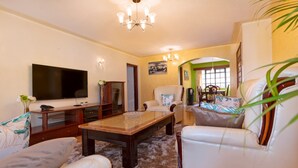 A living room with a flat-screen TV, a wooden coffee table, white leather sofas, and a chandelier.
