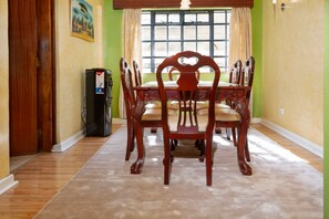 A dining room with a wooden table and chairs, a refrigerator, and a window with curtains. - Bamboo Suites by Edmor suites (Nairobi)