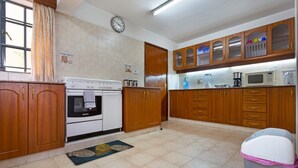 A kitchen with wooden cabinets, a stove, a microwave, and a trash bin.