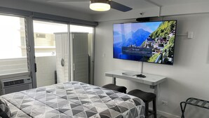 A modern hotel room with a bed, a TV mounted on the wall, a desk, and a chair. - Modern Ocean View Studio - Waikiki Paradise! (Honolulu)