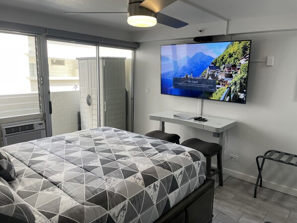 A modern hotel room with a bed, a TV mounted on the wall, a desk, and a chair.