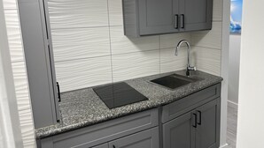 A kitchen with a granite countertop, a stainless steel sink, and grey cabinets. - Modern Ocean View Studio - Waikiki Paradise! (Honolulu)