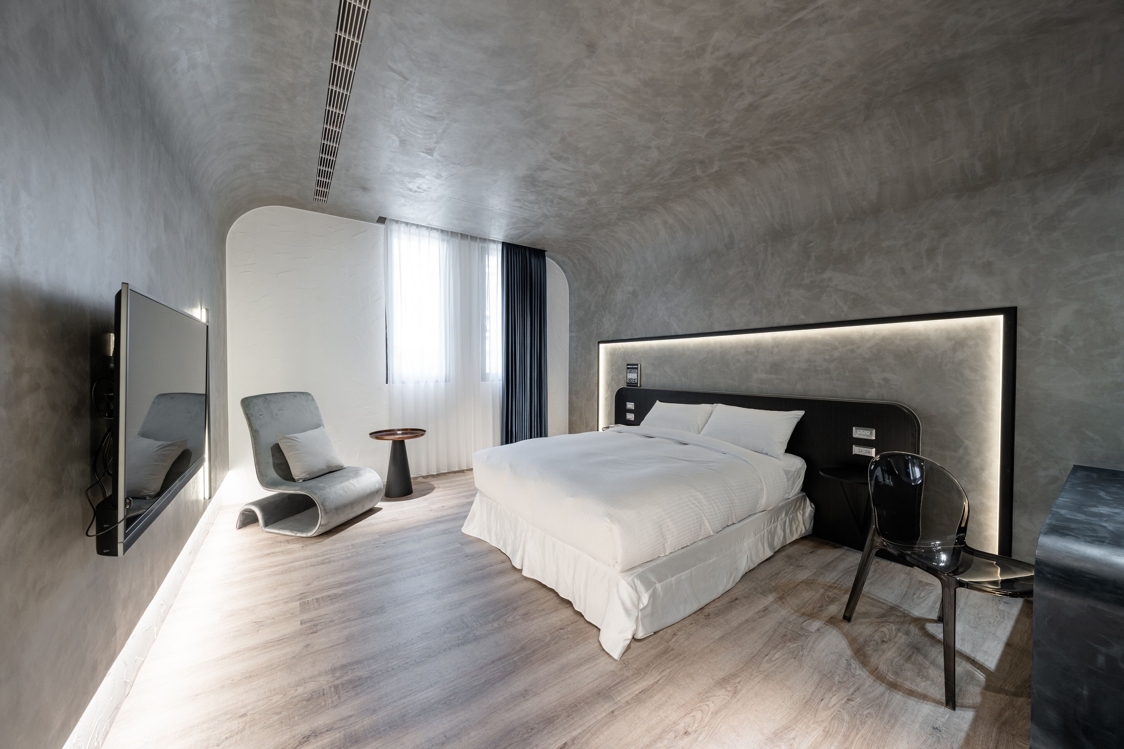 A modern bedroom with a large bed, a chair, a side table, and a mirror.