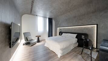 A modern bedroom with a large bed, a chair, a side table, and a mirror.