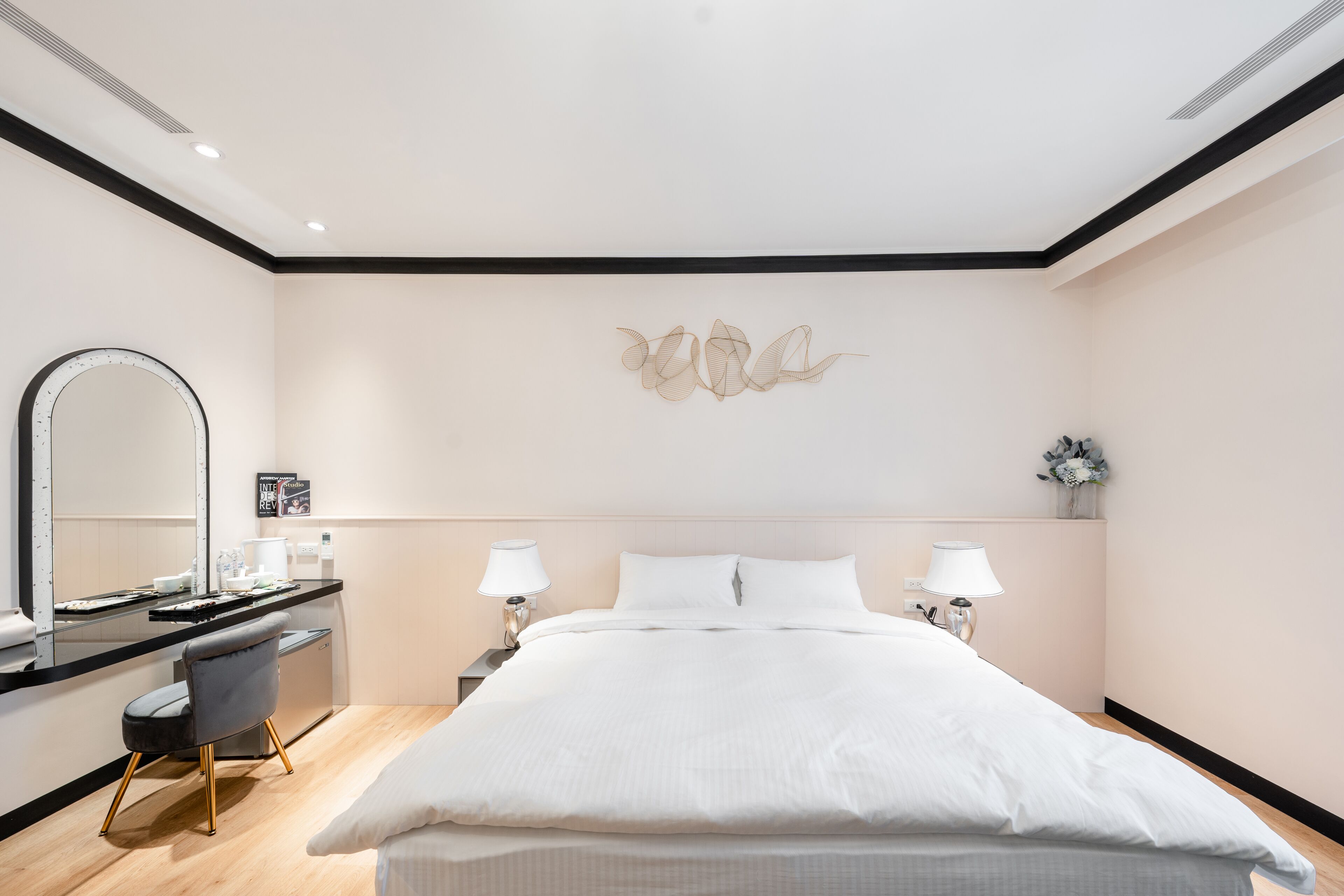 A modern hotel room with a large bed, a desk with a chair, a mirror, and two bedside lamps.