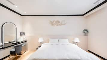 A modern hotel room with a large bed, a desk with a chair, a mirror, and two bedside lamps.