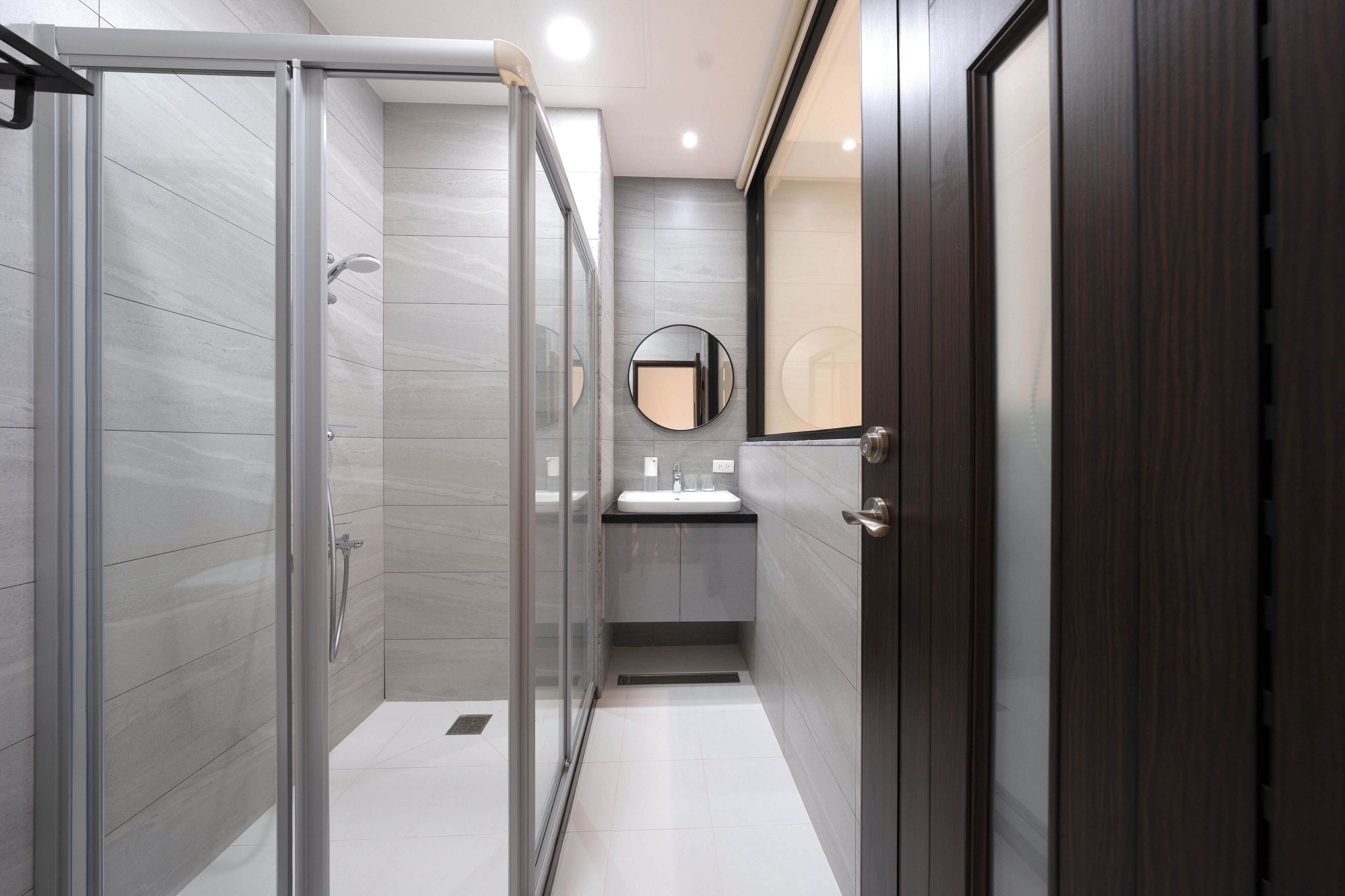 A modern bathroom with a glass shower enclosure, a sink with a mirror, and a dark wooden door.