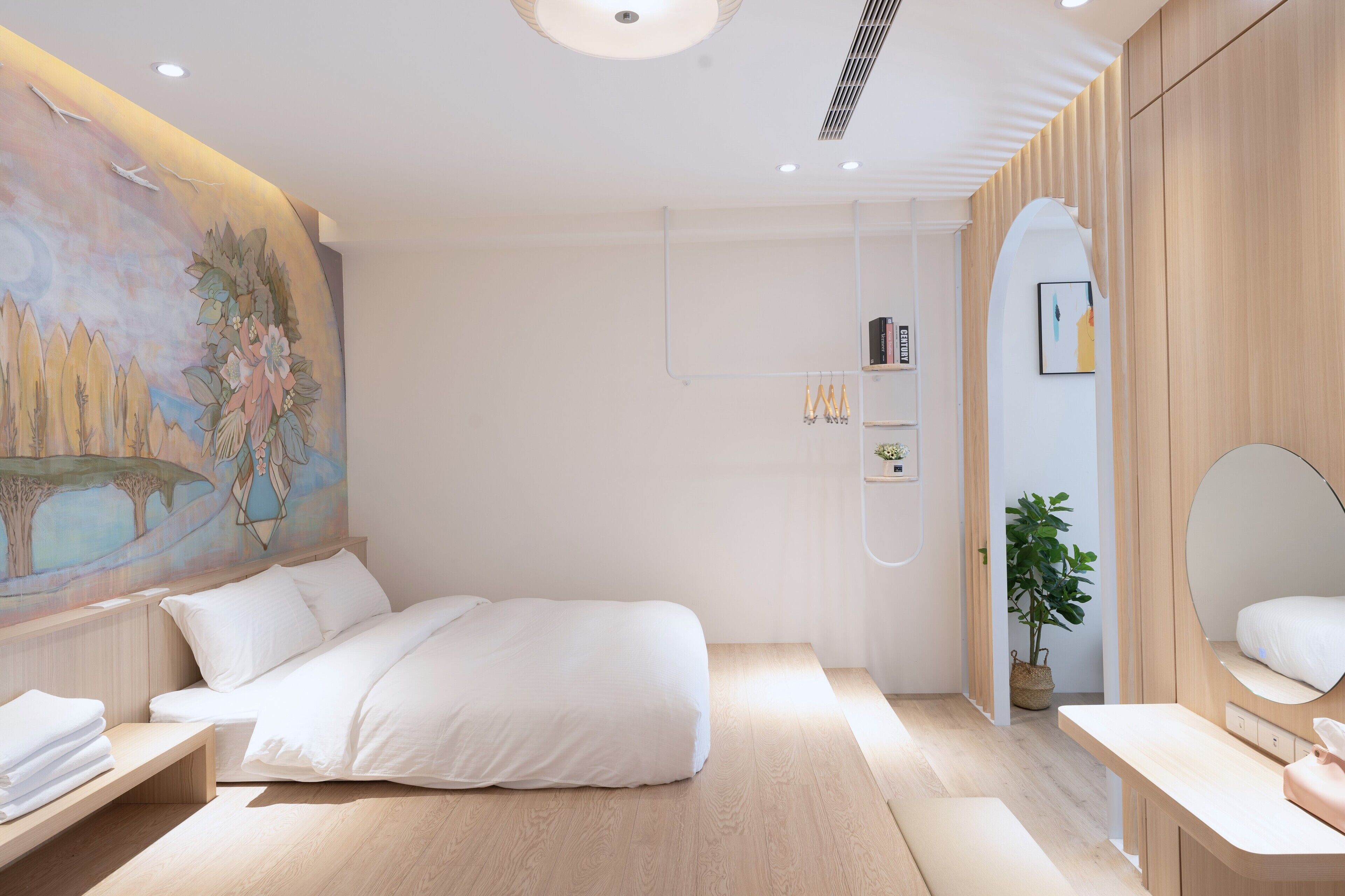 Ein modernes Schlafzimmer mit einem großen Bett, einem Nachttisch, einem kleinen Schreibtisch, einem Spiegel und einem Wandregal.
