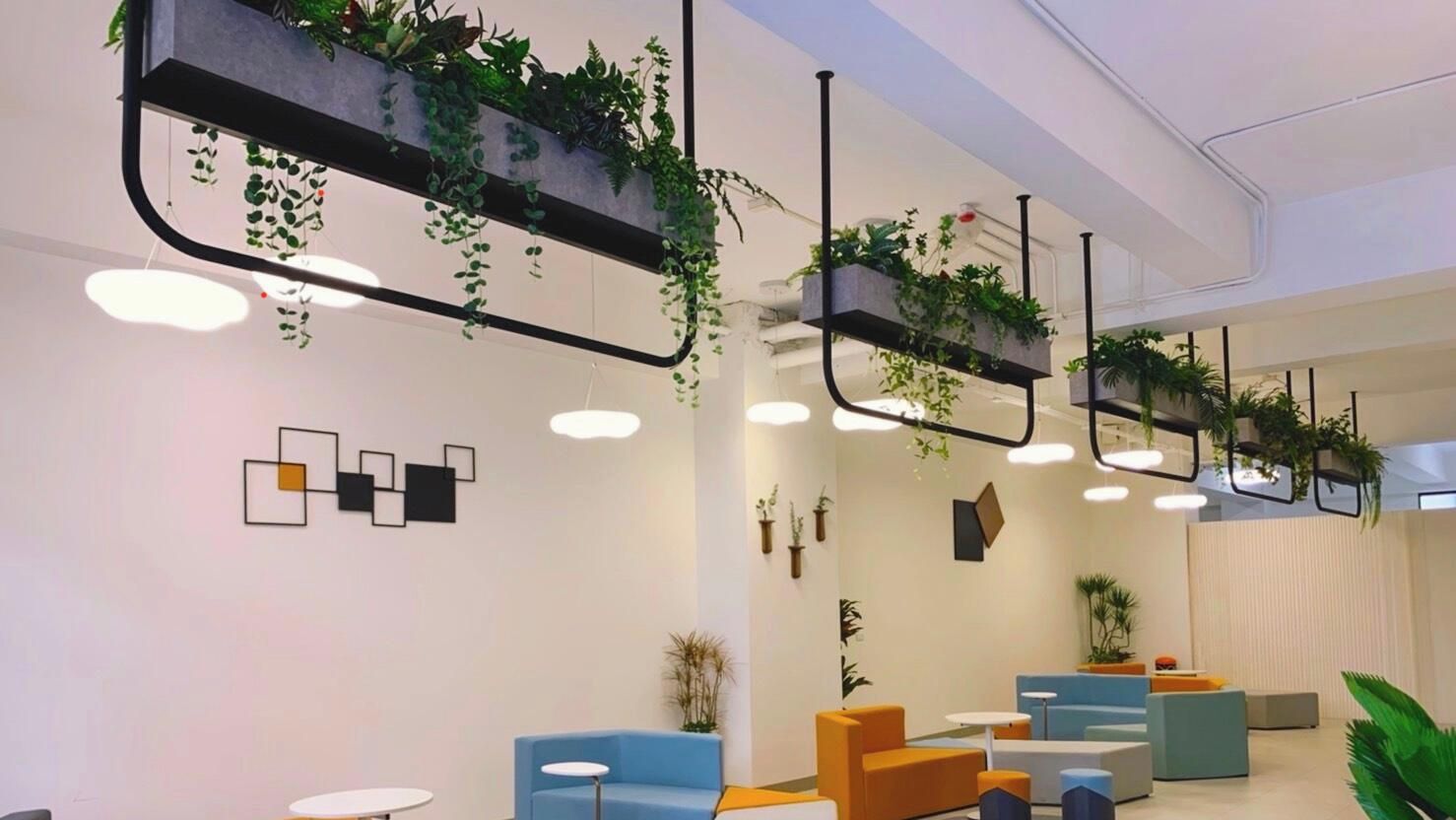 Un intérieur moderne agrémenté d’espaces détente, de plantes suspendues et d’une œuvre d’art murale aux motifs géométriques.