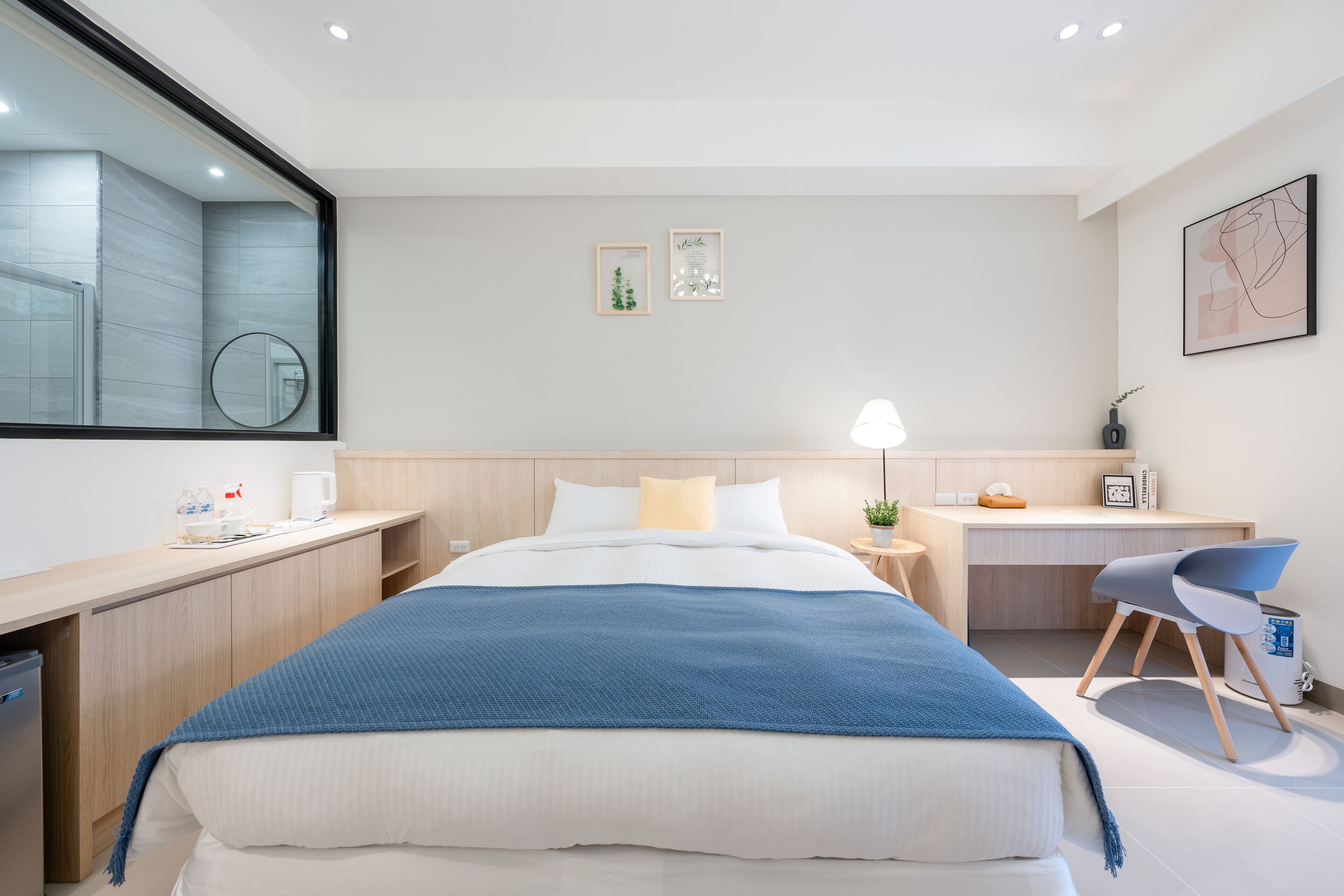 Una habitación de hotel moderna con una cama grande, un escritorio, una silla y una pequeña mesa con una lámpara.