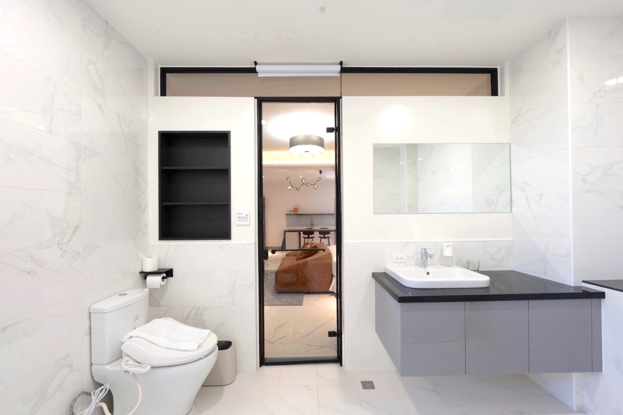 Een moderne badkamer met toilet, wastafel en spiegel. Handdoekrek aanwezig en een plank met toiletartikelen.