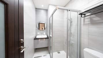 A modern bathroom with a glass shower enclosure, a round mirror, and a dark wooden door.