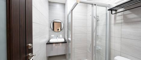 Un baño moderno con cabina de ducha de vidrio, un espejo redondo y una puerta de madera oscura.