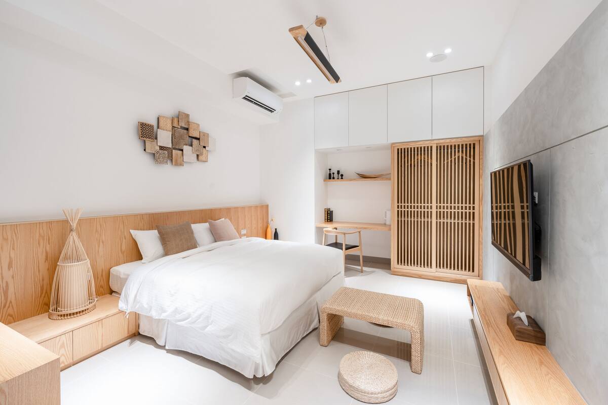 Un dormitorio moderno con una cama grande, mesitas de noche, un banco y un televisor montado en la pared.