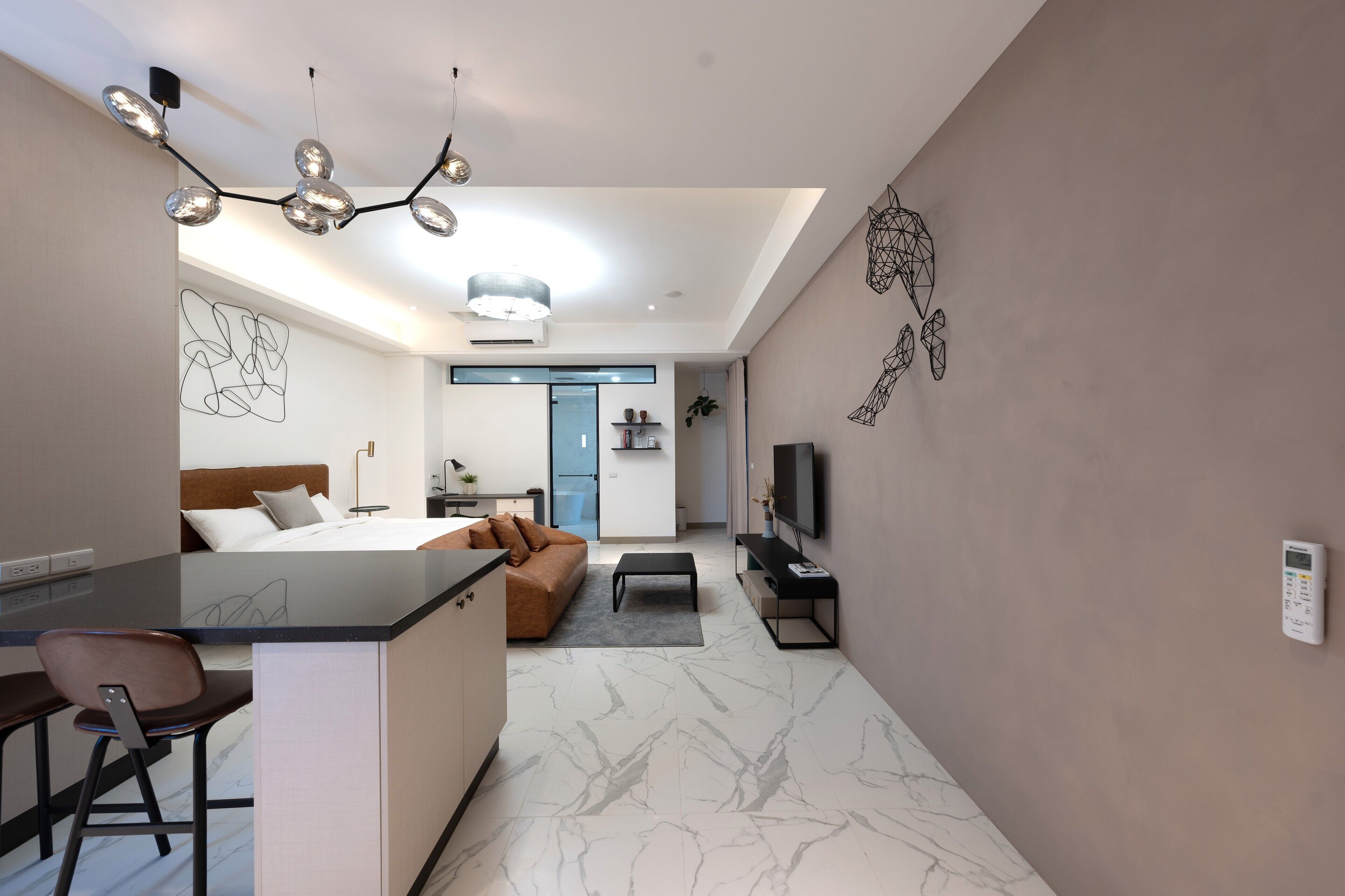 A modern hotel room with a marble floor, a bed with a brown headboard, a desk with a chair, a TV, and a unique wall art piece.