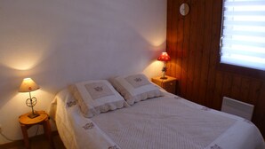 A bedroom with a bed, two bedside lamps, a clock, and a window with blinds. - Cozy apartment, 3 rooms, garden, quiet, near Samoëns center (Samoëns)