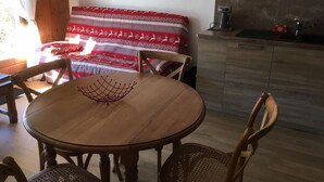 A cozy room with a wooden dining table, chairs, a sofa with a red and white patterned blanket, and a kitchen area with a sink and cabinets. - Cozy apartment, 3 rooms, garden, quiet, near Samoëns center (Samoëns)