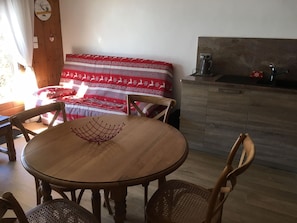 Ein gemütliches Zimmer mit einem Holzesstisch, Stühlen, einer Couch mit einer rot-weißen Decke und einer Küchenzeile mit Spüle und Schränken.