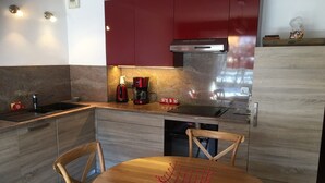 A modern kitchen with a built-in oven, a coffee maker, and a dishwasher. There is a wooden dining table with chairs. - Cozy apartment, 3 rooms, garden, quiet, near Samoëns center (Samoëns)