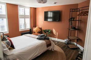 Een slaapkamer met een bed, een televisie, een plank met kleding en een radiator.
