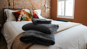 A neatly made bed with folded towels and a quilted pillow in a room with exposed brick walls and a window. - Cathedral Superior Apartment (Worcestershire)