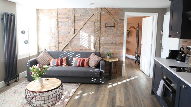 A modern living room with a grey sofa, a round coffee table, and a brick wall. - Cathedral Superior Apartment (Worcestershire)