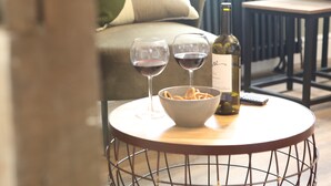 A round table with a bowl of snacks, two wine glasses, and a bottle of wine.