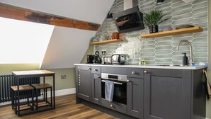 A modern kitchen with dark cabinetry, a built-in oven, and a microwave. There is a wooden table and a window providing natural light.