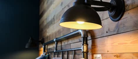 A wall-mounted lamp with a metal head and a black cord, a wooden wall with a visible grain pattern, and a sign with the word "gracious!"