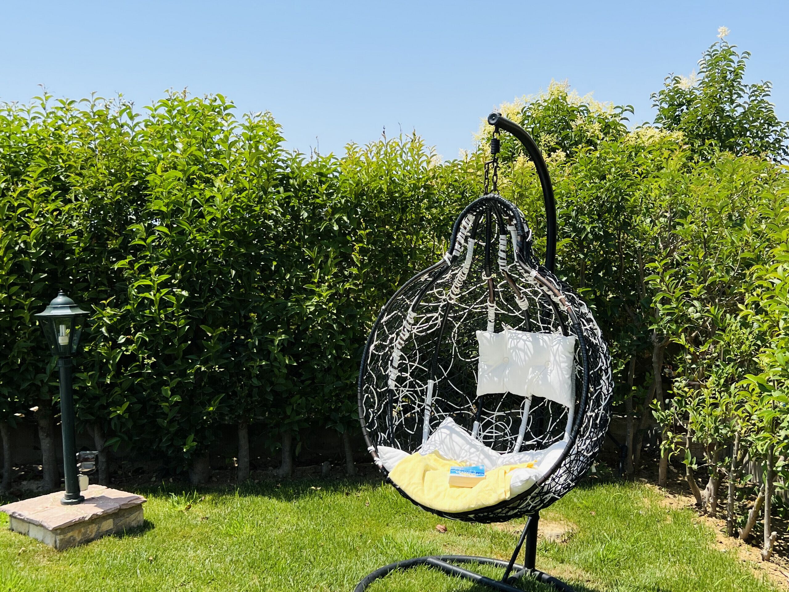 A hanging egg chair in a garden with a lamp post and a hedge in the background.