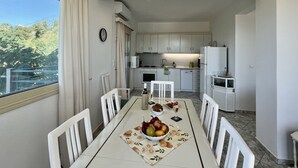A dining area with a table set for four, a kitchen in the background, and a view of greenery outside. - Villa Emiliata (Spartia)