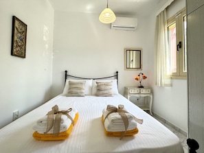 A neatly made bed with two towels tied with ribbons, a bedside table with a lamp, and a window with curtains.