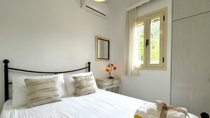 A neatly made bed with white linens and striped pillows, a bedside table with a lamp, and a window with curtains. - Villa Emiliata (Spartia)