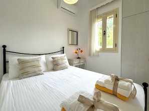 A neatly made bed with white linens and striped pillows, a bedside table with a lamp, and a window with curtains.