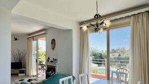 A dining area with a table set for two, a sofa, and a view of a pool and greenery outside. - Villa Emiliata (Spartia)