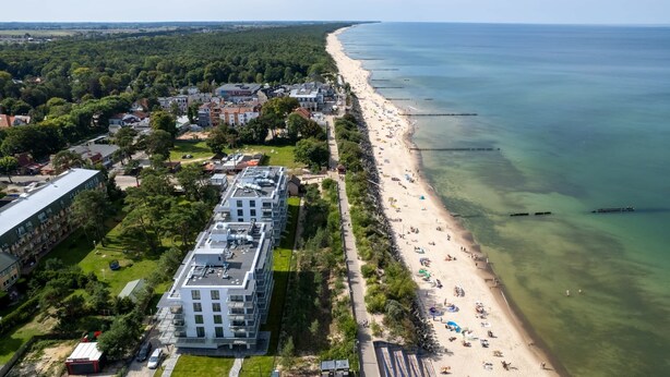 An aerial view of a coastal town with a beach, buildings, and greenery.
