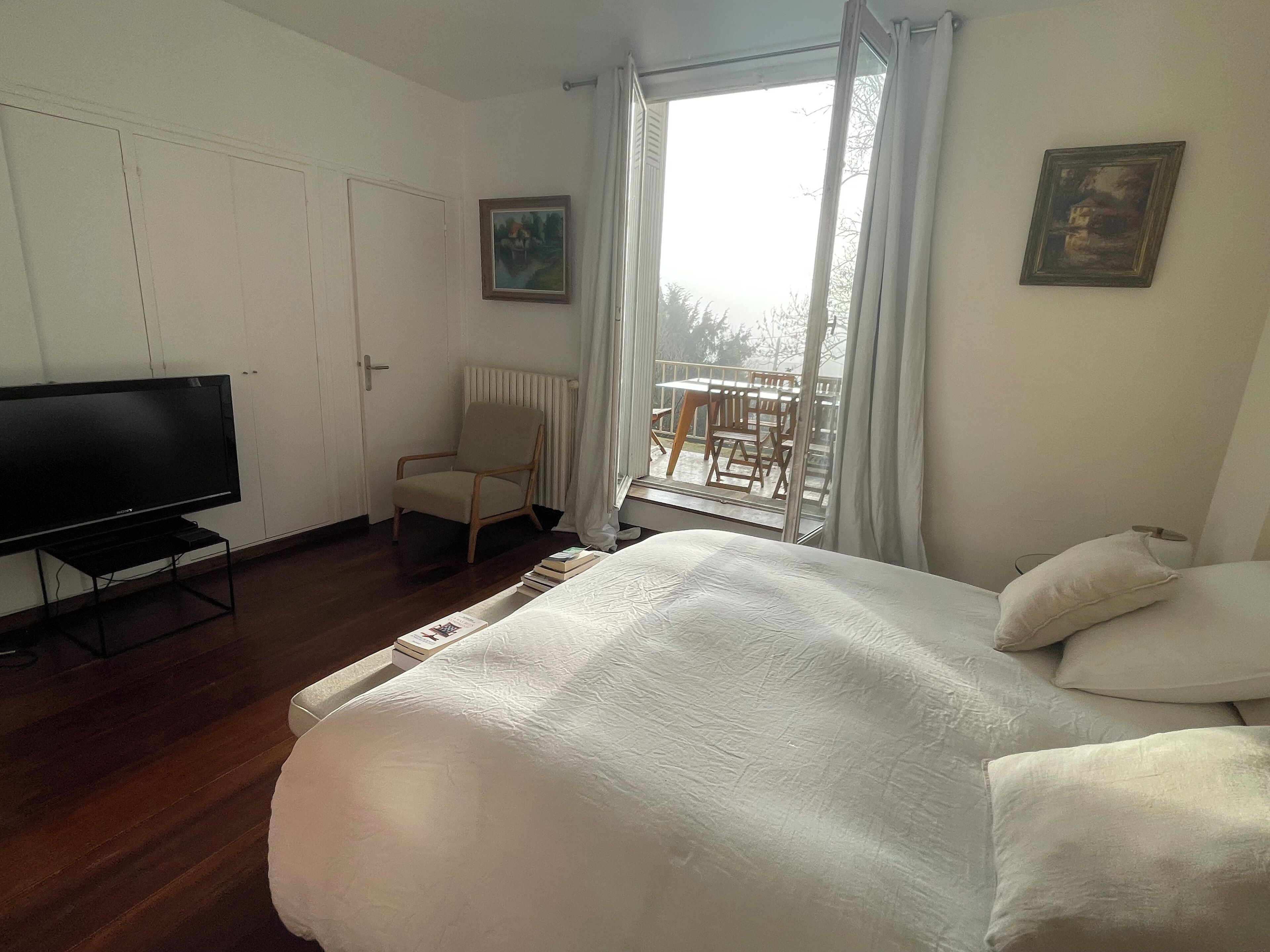 Een hotelkamer met een bed, een televisie, een stoel, een raam met gordijnen en een schilderij aan de muur.