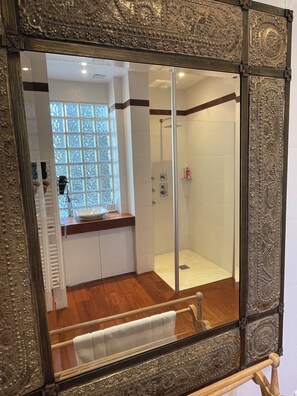 Ein Badezimmer mit Duschkabine aus Glas, Waschbecken und einem Fenster mit satinierten Glasscheiben.
